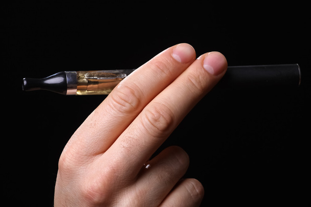 Ręka trzyma elektroniczny papieros na czarnym tle - Zdjęcie, obraz