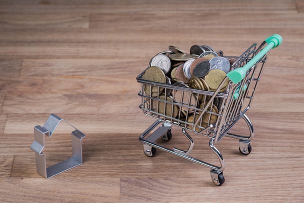 Shopping cart with house and coins on the wooden table - Fotografie, Obrázek