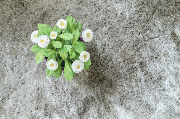 Κοντινά πλάνα τεχνητό φυτό με λευκό λουλούδι σε μωβ κατσαρόλα σε γκρι χαλί υφή φόντο στην κορυφή θέα - Φωτογραφία, εικόνα