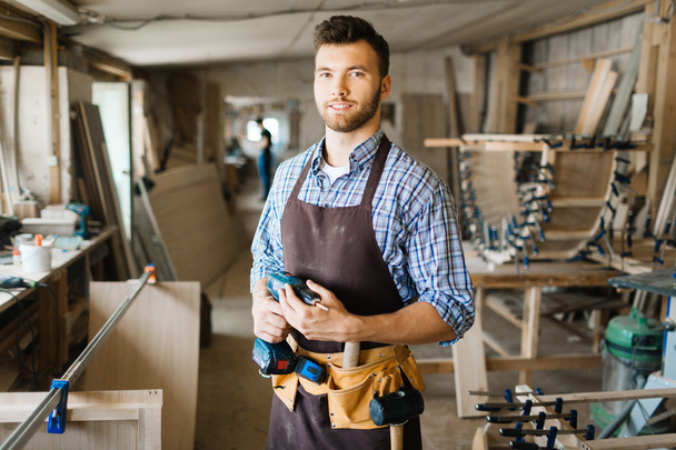 Плотник-мужчина с дрелью в мастерской
 - Фото, изображение