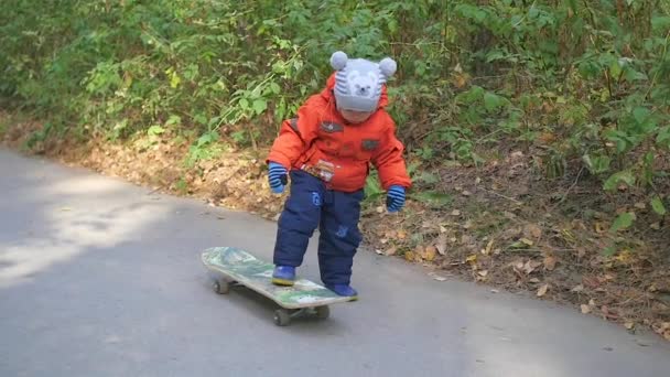 egy kisgyerek megtanulja, hogy lovagolni a gördeszka a parkban - Felvétel, videó