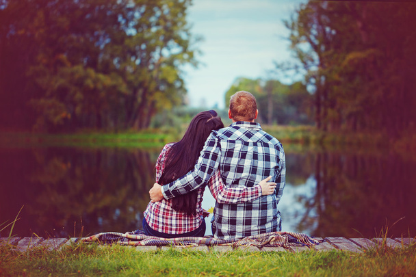  Loving couple in autumn park sitting on the beach, river or lak - Фото, изображение