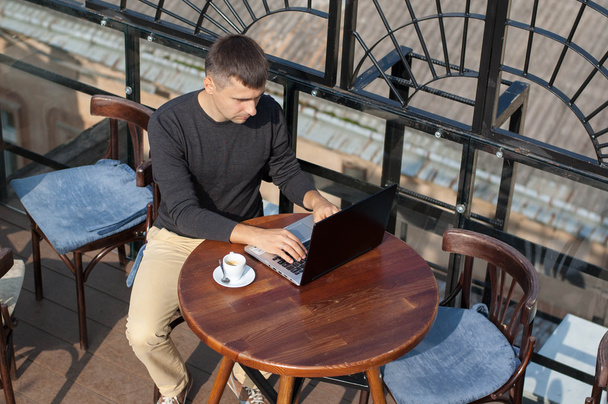 Mann mit Laptop sitzt an einem Tisch im Freien. - Foto, Bild