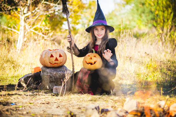 Happy Halloween. Cute little witch with a pumpkin in the hands of the fire. - Photo, Image