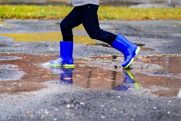 Menino de borracha botas de chuva azuis pulando para poça suja
 - Foto, Imagem