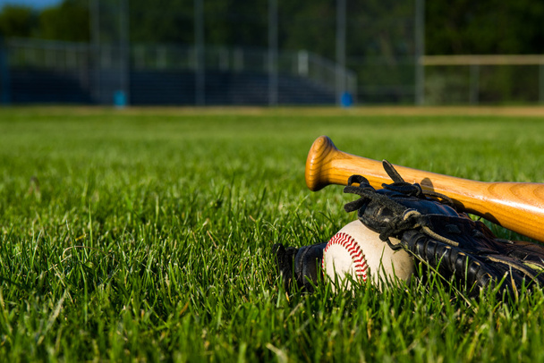 Uma bola de basebol, luva e morcego num diamante de basebol, com um estádio ao fundo
 - Foto, Imagem