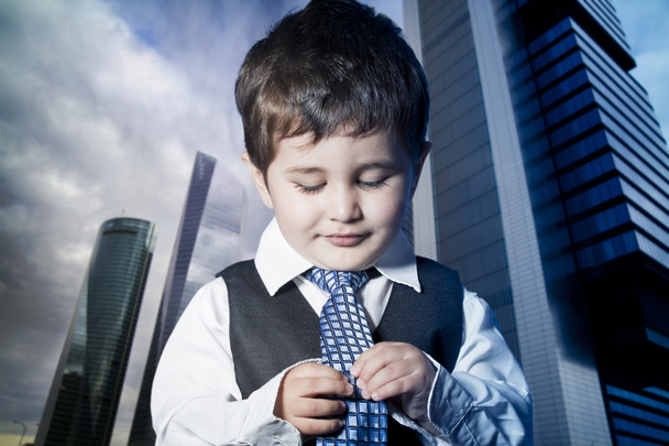 criança vestido homem de negócios com as mãos em sua gravata e arranha-céus
 - Foto, Imagem