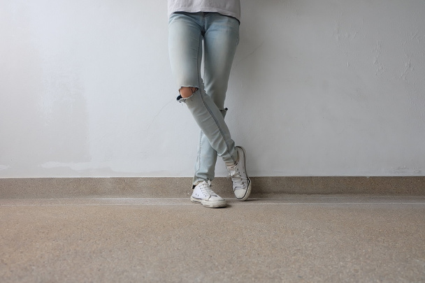 junge Modefrau in blauen Jeans und weißen Turnschuhen auf dem Boden  - Foto, Bild