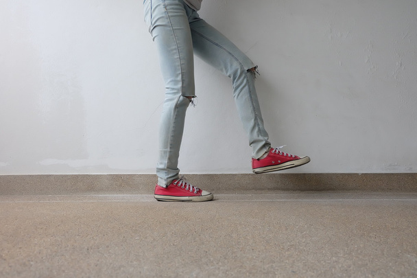 Young Fashion Woman's Legs in Blue Jeans and Red Sneakers on Floor  - Foto, imagen
