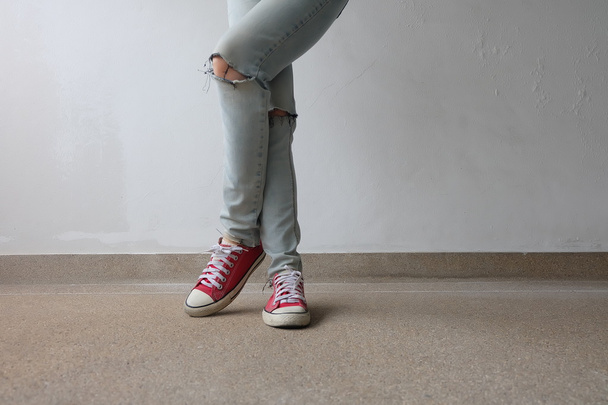 Молода мода жінка ноги в синіх джинсах і червоні кросівки на підлозі  - Фото, зображення