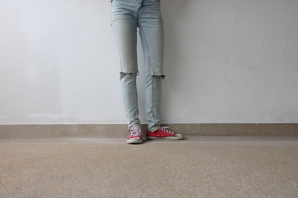 Pernas de mulher de moda jovem em calças de ganga azuis e tênis vermelhos no chão
  - Foto, Imagem