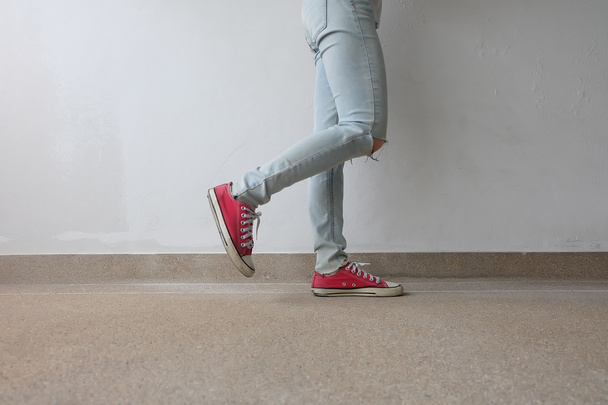 Młoda Moda Woman nogi w niebieskie dżinsy i czerwone sneakers na podłodze  - Zdjęcie, obraz