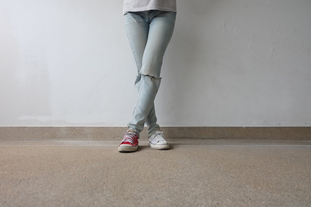 Młoda Moda Woman nogi w niebieskie dżinsy i białe, czerwone sneakers na podłodze  - Zdjęcie, obraz