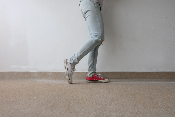 Young Fashion Woman's Legs in Blue Jeans and White, Red Sneakers on Floor  - Foto, Bild