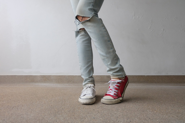 若いファッションの女性の足は、ブルージーンズと白、床に赤いスニーカー  - 写真・画像