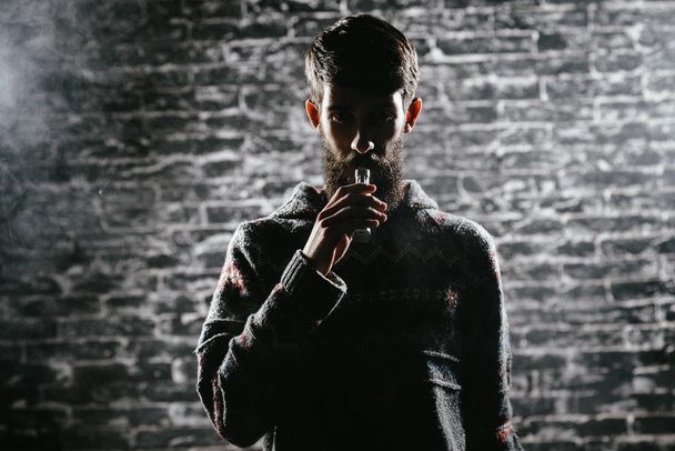 Un joven con barba vapeando un cigarrillo electrónico. Vaporizador de humo Vaper hipster
. - Foto, imagen
