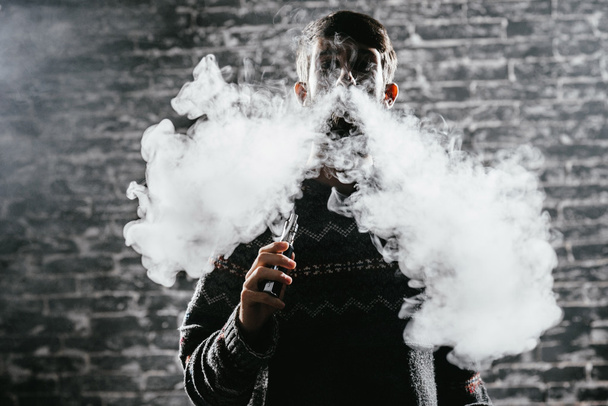 Young man with beard vaping an electronic cigarette. Vaper hipster smoke vaporizer. - 写真・画像