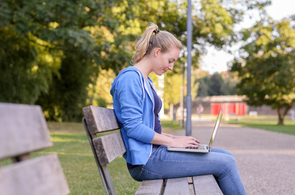 Genç kadın rahatlatıcı bir dizüstü bilgisayar kullanarak bir parkta - Fotoğraf, Görsel