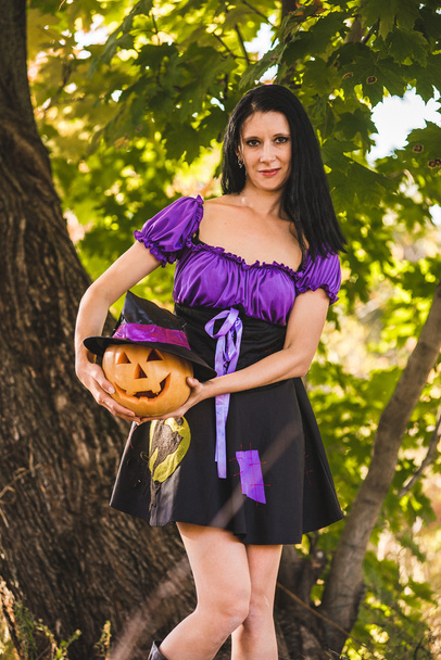 Jonge vrouw in Halloween kostuum in de herfst bos met gele pompoen witch. - Foto, afbeelding