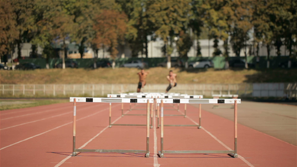 Two sprinters jumping over five hurdles on runways - Materiał filmowy, wideo