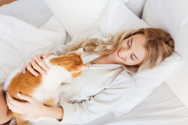 happy young woman with cat in bed at home - Фото, зображення