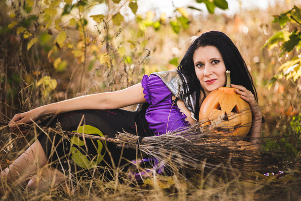 Mujer joven en disfraz de bruja de Halloween en el bosque de otoño con calabaza amarilla
. - Foto, imagen