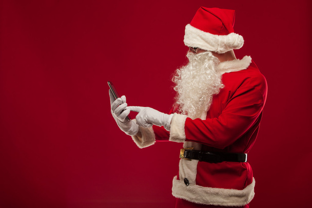 Modern Santa Claus using tablet pc over red background. Christma - Foto, imagen