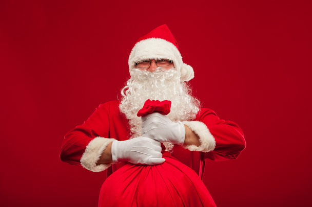 Санта-Клаус с большой сумкой на плечах очки красный фон
 - Фото, изображение