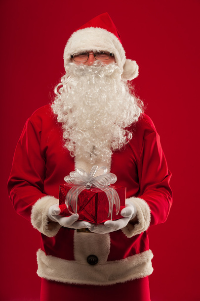 Photo of kind Santa Claus giving xmas present and looking at cam - Foto, afbeelding