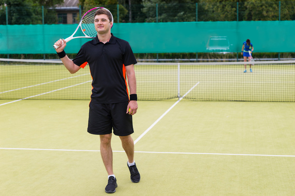 Happy male tennis player holding a racket on his shoulder after  - Fotó, kép