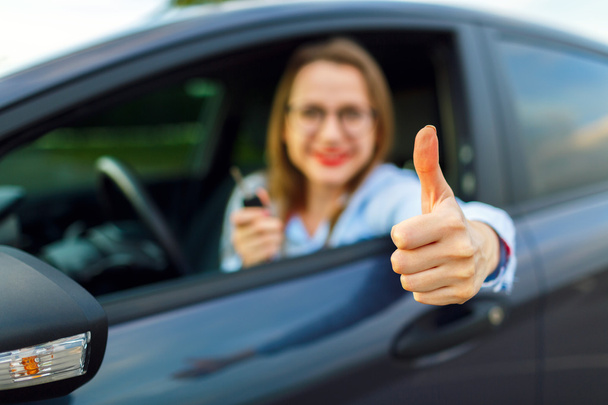 Joven mujer feliz sentado en un coche con el pulgar hacia arriba
 - Foto, imagen