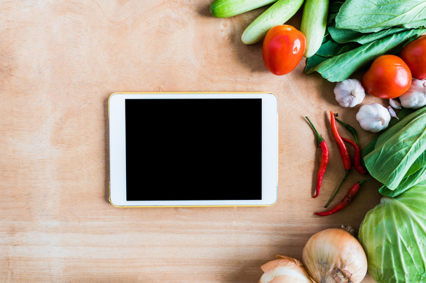 Bovenaanzicht van verse groenten met tablet touch computer gadget op houten tafel achtergrond. - Foto, afbeelding