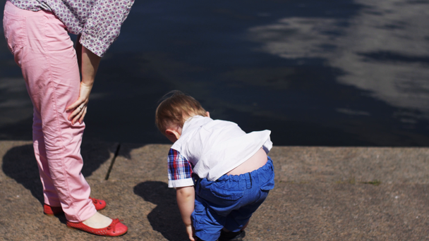 Matka a malý syn odkládat boty na nábřeží. Událost. Letní slunečný den. Voda. - Záběry, video