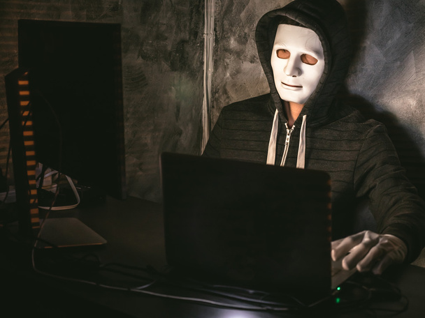 Компьютерный хакер - человек в толстовке с маской крадет данные с ноутбука
 - Фото, изображение