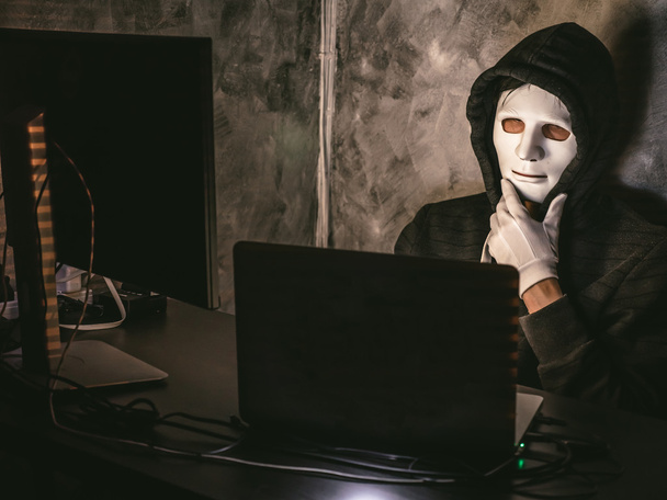 Computerhacker - Mann im Kapuzenshirt mit Maske stiehlt Daten aus Laptop - Foto, Bild