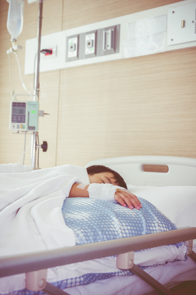 Garçon asiatique allongé sur un lit de malade avec perfusion intraveineuse saline (IV). Les soins de santé et les personnes concept
.  - Photo, image