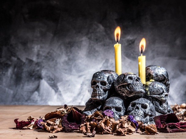 Totenköpfe mit brennenden Kerzen und getrockneten Blumen auf dunklem Hintergrund. - Foto, Bild