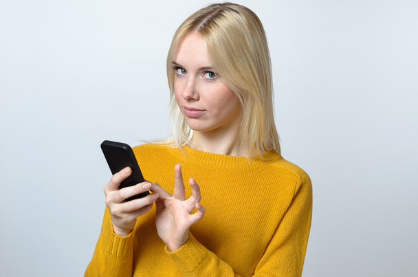 Mladá žena při pohledu na fotoaparát s mobilním telefonem - Fotografie, Obrázek