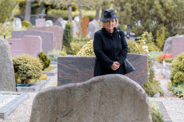 Senior dame in rouw op een graveside - Foto, afbeelding