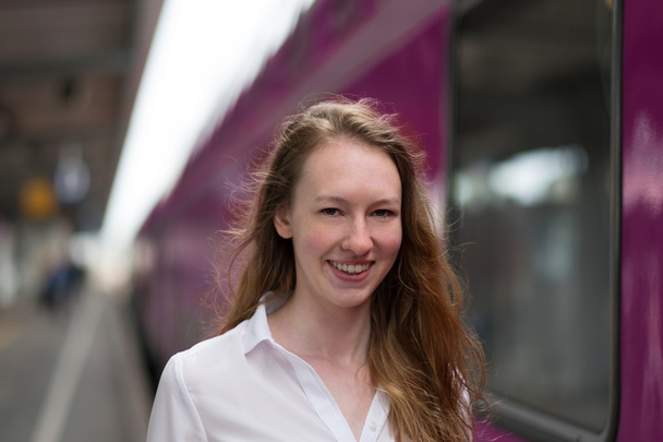 Hymyilevä nainen seisomassa rautatieaseman laiturilla
 - Valokuva, kuva
