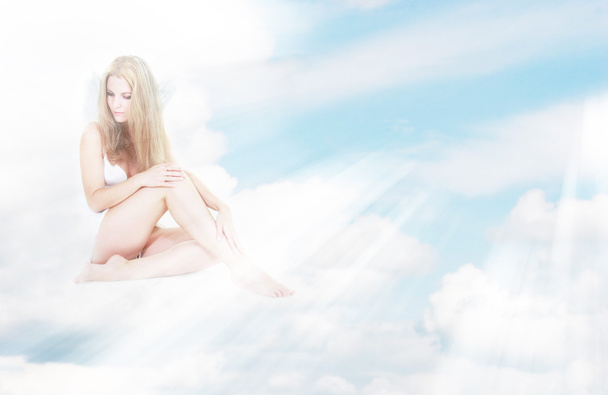 alleen engel meisje in de stralen van de zon zitten op wolken - Foto, afbeelding