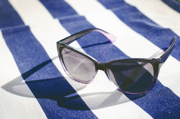 Battaniyenin üzerine siyah aynalı güneş gözlüğü. Gözlükten gölge. Güneş ışığı. Yaz konsepti  - Fotoğraf, Görsel