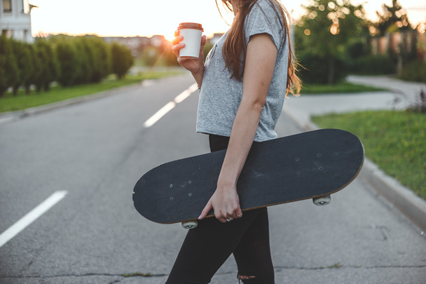 beautiful girl drinks from white to-go cup holding skateboard - Foto, imagen