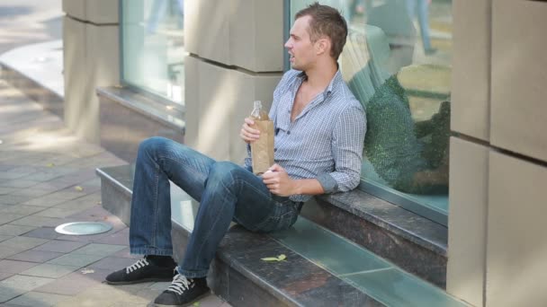 részeg férfi fekszik a járdán kívül. az ember iszik sört egy papír porzsák - Felvétel, videó