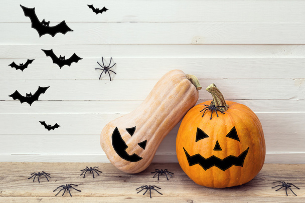 Two pumpkins with painted faces, decorative spiders and bats on  - 写真・画像
