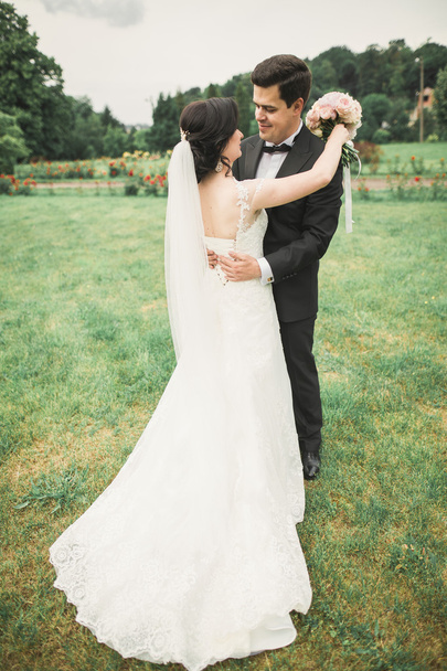 Stylish couple of happy  newlyweds walking in the park on their wedding day with bouquet - Foto, Imagen