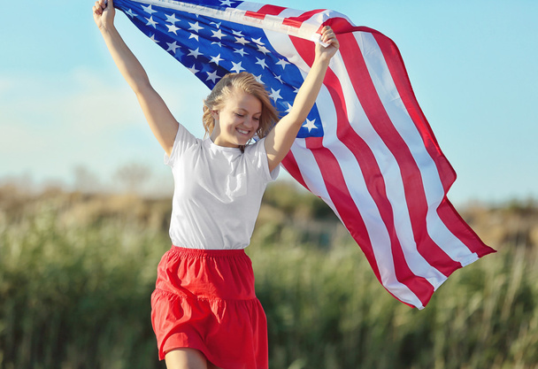 Young woman holding American flag on blue sky background - Photo, Image