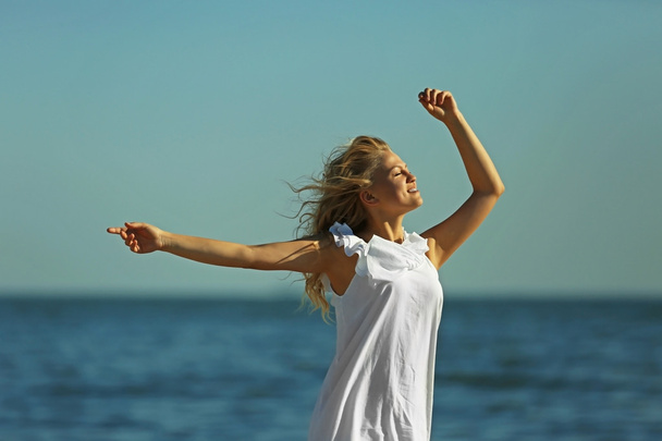 Young woman raising hands on blue sky background - Foto, Imagem