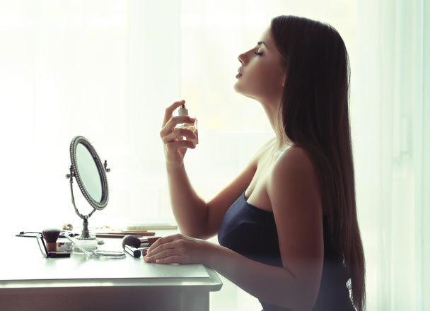 Beautiful young woman looking in mirror while using perfume - Foto, Imagem