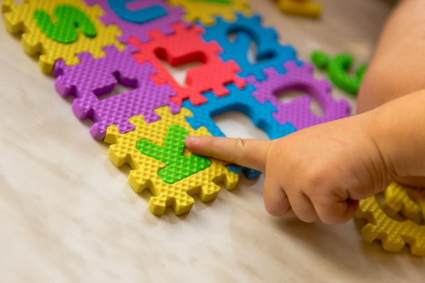 Colorful foam puzzle letters and numbers in kid's hands on a light table - Foto, imagen